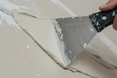Ręka z kielnią wygładza masę szpachlową podczas gipsowania ścian.