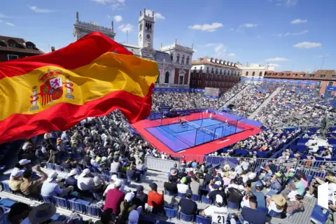 Bandiera spagnola sventola su un campo da padel gremito di spettatori. Atmosfera vibrante per il padel in Spagna.