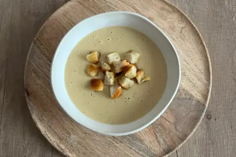 Aksamitna zupa cebulowa krem, udekorowana chrupiącymi grzankami, podana na drewnianej desce.