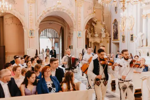 Muzycy grają pieśń na wejście w kościele. W tle para młoda wchodzi do świątyni.