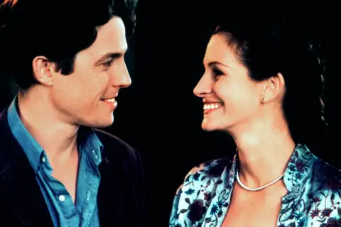 Uśmiechnięta obsada Notting Hill: Hugh Grant i Julia Roberts patrzą na siebie z czułością.