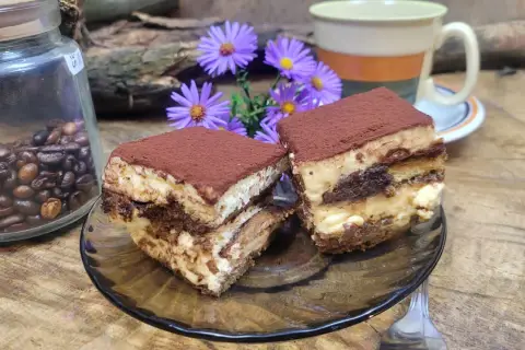 Dwa kawałki tiramisu, idealne ciasto do kawy, obok słoika z ziarnami kawy i fioletowych kwiatów.