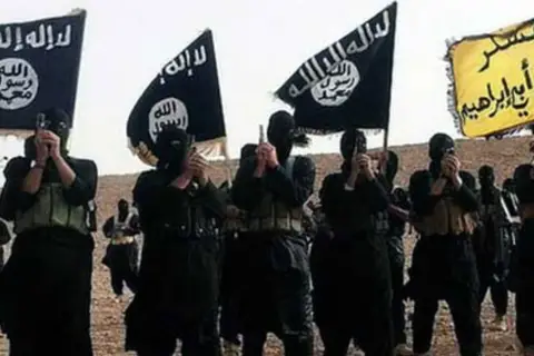 Grupa uzbrojonych mężczyzn w czarnych ubraniach i maskach, trzymających flagi z arabskim napisem, symbolizujące dżihad.