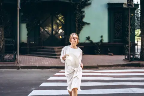 Dziewczyna w białej sukience i kapeluszu przechodzi przez pasy. Stylizacja sugeruje, że to marka MSGM.