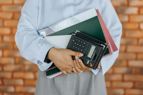 Osoba trzyma stos dokumentów i kalkulator. Idealne do usług fotograficznych, gdzie liczy się każdy szczegół, także VAT.