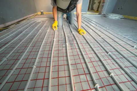 Instalator układa rury do ogrzewania podłogowego. Dokładna ilość metrów rury na m2 podłogówki zależy od projektu.