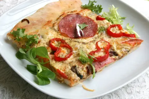 Kawałek pizzy z salami, papryką i serem na białym talerzu.