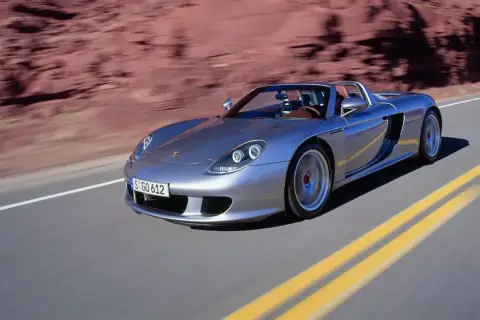 Srebrny Porsche Carrera GT pędzi po pustynnej drodze, zostawiając za sobą rozmyte czerwone skały.