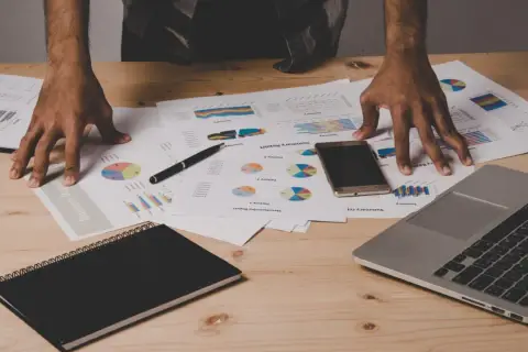Ręce nad dokumentami z wykresami i raportami, laptop, telefon i notatnik. Analiza danych i data warehouse design.