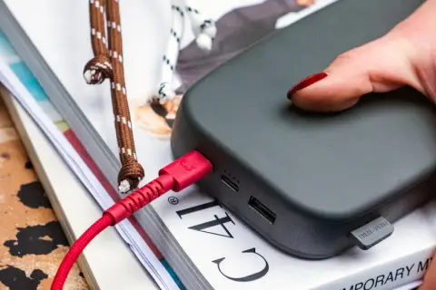 Dłoń z czerwonym lakierem podłącza czerwony kabel do powerbanku, zapewniając szybkie ładowanie.