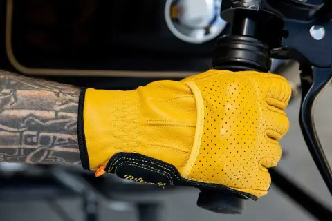 Mano tatuata con guanti Biltwell gialli traforati, pronti per un giro in moto.