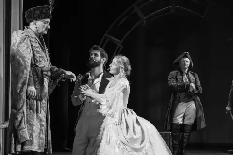 Aktorzy w historycznych strojach na scenie. W centrum młoda para, obok nich starszy mężczyzna w bogatym stroju. To piękny **teatr u przyjaciół**.