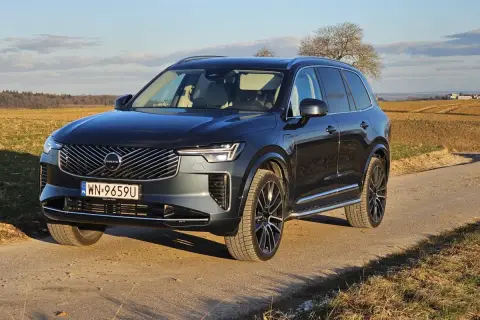 Ciemnoszary Volvo XC90 T8 na drodze polnej, z polami i drzewami w tle.