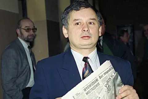 Jarosław Kaczyński z gazetą, zastanawia się, kto ze starej gwardii PiS trafił na "czarną listę". Obok mężczyzna w okularach.