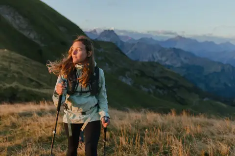 Kobieta z kijkami do **speed hikingu** podziwia alpejski krajobraz o zachodzie słońca.