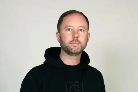 Daniel Holmgren, en man med blå ögon och skägg, bär en svart huvtröja.