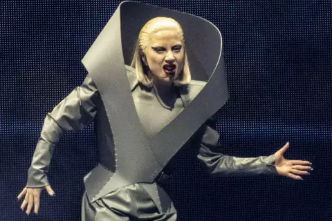 Lady Gaga w szarym, futurystycznym stroju na koncercie w Polsce, z charakterystycznym kołnierzem i makijażem.