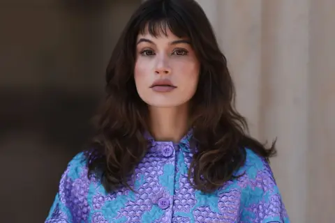 Mujer con melenas cortas con volumen, flequillo y un llamativo abrigo morado y turquesa.