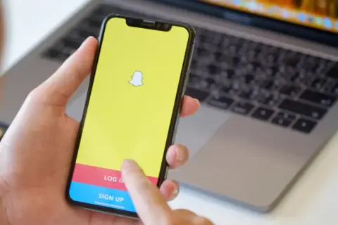 Dłoń trzyma smartfon z logo Snapchata. Widoczny ekran logowania, który może pomóc w procesie jak usunąć konto na snapie.