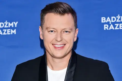 Rafał Brzozowski w czarnym garniturze na niebieskim tle z napisem "Bądźmy razem".