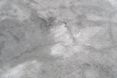 Szara, chropowata powierzchnia betonu z licznymi, cienkimi pęknięciami. Ten popękany chudziak opowiada historię czasu i warunków atmosferycznych.