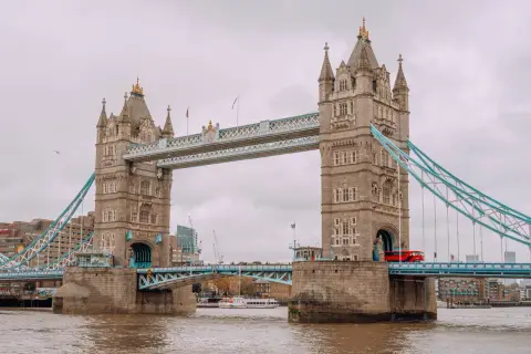 Tower Bridge w Londynie, symbol miasta, opowiada swoją historię. Czerwony autobus przejeżdża przez most, a w tle widać nowoczesne budynki.