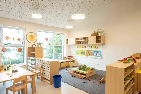 Helle, kindgerechte Reggio Raumgestaltung Kita mit Holzelementen, Spielzeug und einem Geburtstagsbanner.