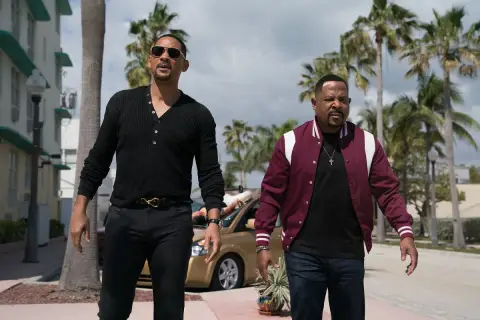 Will Smith i Martin Lawrence w filmach "Bad Boys" idą ulicą w słoneczny dzień, otoczeni palmami.