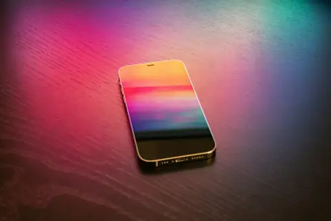 Złoty iPhone z kolorowym ekranem na drewnianym blacie. Dowiedz się, jak wgrać dzwonek na iPhone bez iTunes.