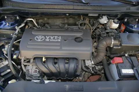 Silnik VVT-i 16 Valve z Toyoty Corolla E12. Widoczny alternator, akumulator i elementy układu dolotowego.