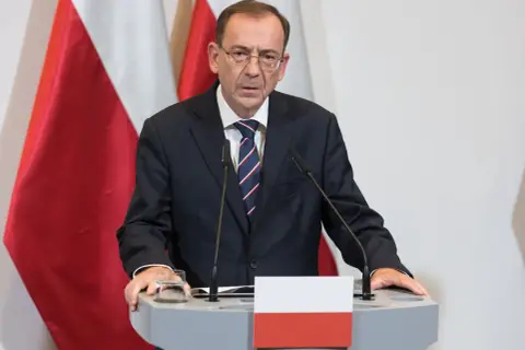 Mężczyzna w garniturze przy mównicy z polską flagą. Czy to odpowiedź na pytanie, dlaczego prezydent nie skorzystał z prawa łaski wobec skazanych urzędników państwowych?