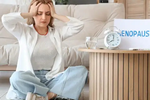 Kobieta z bólem głowy podczas menopauzy, obok tabletki i budzik.