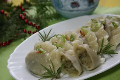 Pyszne, domowe pierogi ukraińskie, udekorowane szczypiorkiem i rozmarynem, prezentują się apetycznie na białym talerzu.