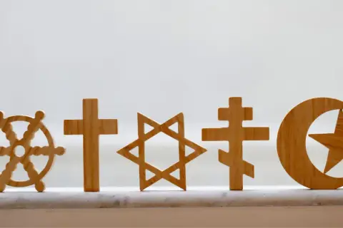 Drewniane symbole religijne: koło Dharmy, krzyże, Gwiazda Dawida, półksiężyc z gwiazdą. Pokazują różnorodność wierzeń, jak w Bangladeszu religia.