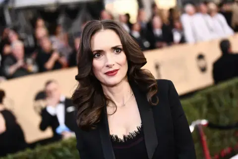 Winona Ryder w czarnej marynarce, z burzą brązowych włosów. Wygląda jakby opowiadała o swoich dzieciach.