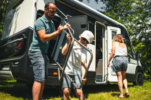Un père et son fils sortent une chaise pliante de leur camping-car, prêts pour une aventure en Ardeche.