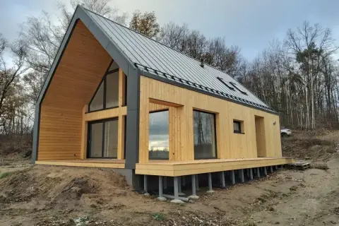 Nowoczesny dom pasywny z drewnianą elewacją i dużymi oknami, otoczony lasem.