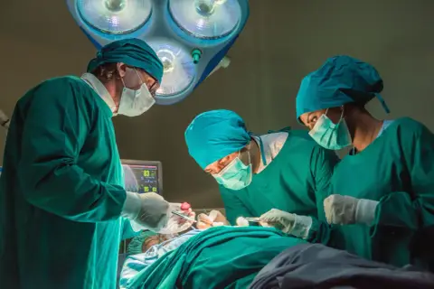 Trzech chirurgów w zielonych fartuchach i maseczkach skupionych na pacjencie. Zastanawiasz się, ile zarabia chirurg?