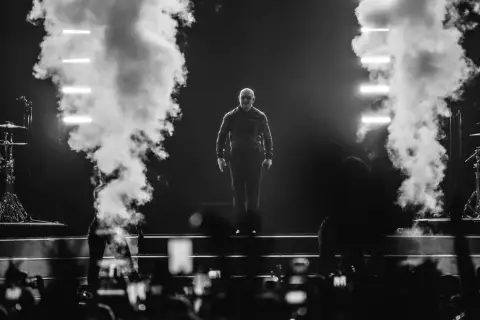 Pitbull na scenie, otoczony dymem i światłami, podczas koncertu.