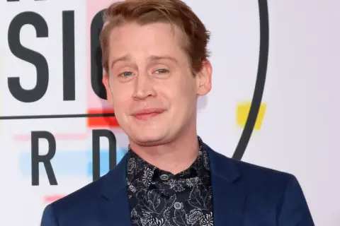 Macaulay Culkin, żyje i ma się dobrze, pozuje na tle napisu "MUSIC AWARDS".