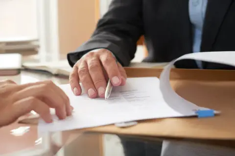 Dwie osoby analizują dokumenty. Jedna z nich wskazuje piórem na tekst, być może ustalając alimenty do 10 każdego miesiąca.
