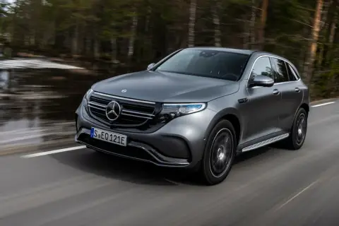 Szary Mercedes EQC jedzie po drodze wśród drzew.