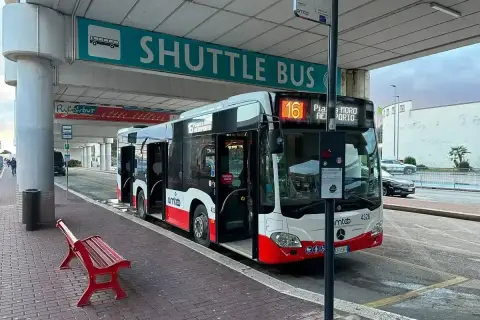 Autobus wahadłowy na **bari lotnisko** czeka na pasażerów pod znakiem "SHUTTLE BUS". Czerwona ławka stoi obok.