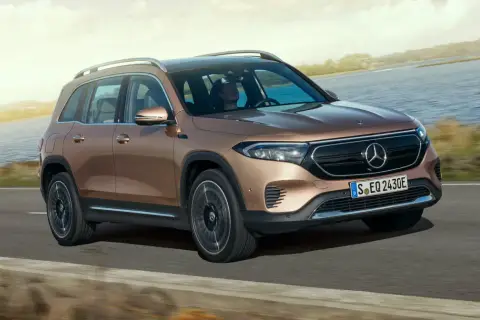 Brązowy Mercedes EQB jedzie po drodze nad jeziorem.