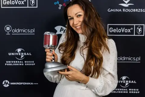 Uśmiechnięta kobieta z mikrofonem-statuetką. Jej stylizacja i nagroda sugerują, że to inspiracja dla tych, którzy chcą dowiedzieć się, jak zostać dubbingiem.