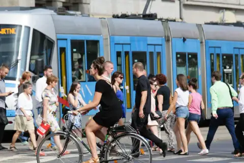 Ludzie przechodzą przez pasy, obok tramwaju z napisem "79 POŚWIETNE". To typowy widok wrocławskiego kod boczny pojazdu.