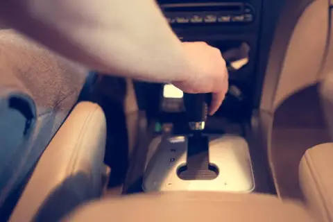 Dłoń kierowcy na dźwigni zmiany biegów. W samochodzie zainstalowana jest blokada alkoholowa, która wymaga dmuchnięcia przed jazdą.