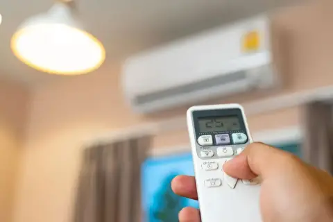 Mano sujetando control remoto para aire acondicionado, ajustando temperatura. Mantenimiento aire acondicionado para confort.