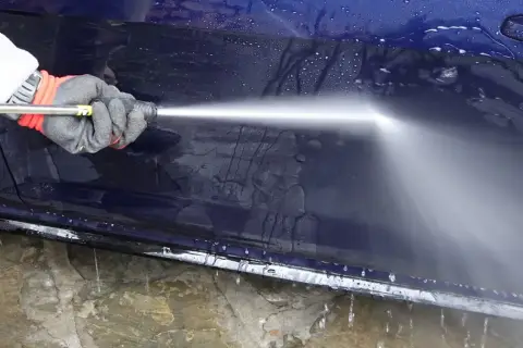 Rękawica z pianką i myjka ciśnieniowa pokazują, jak myć auto na myjni. Woda spływa po ciemnoniebieskim lakierze.
