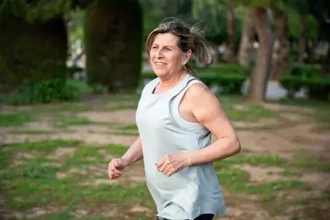 Uśmiechnięta kobieta w średnim wieku cieszy się bieganiem 5 km dziennie w parku.